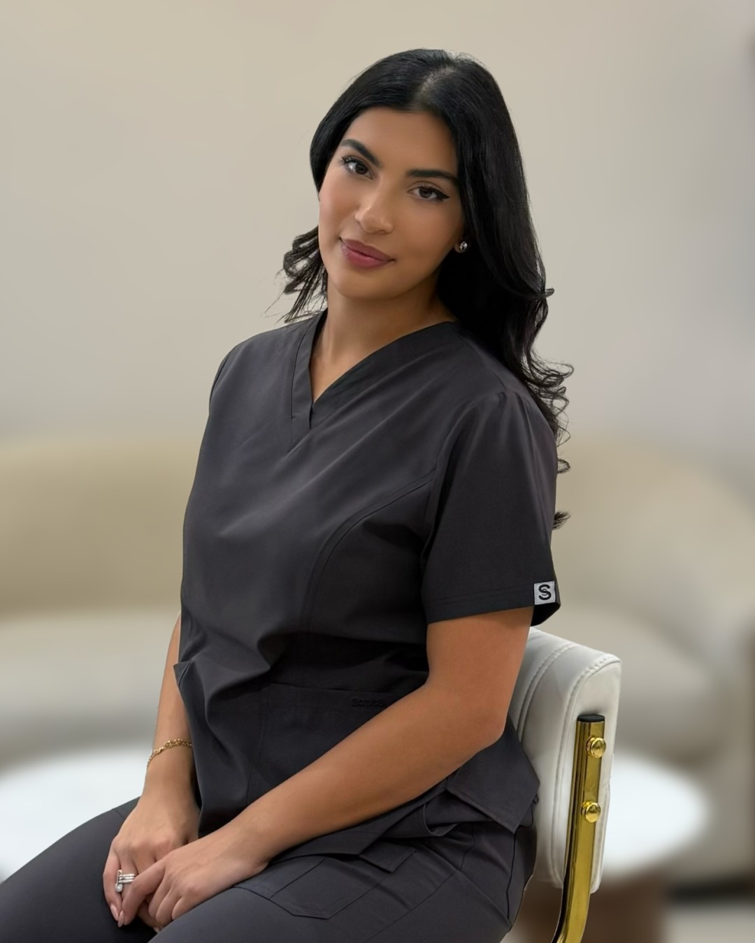 Ranna seated in clinic, wearing charcoal scrubs